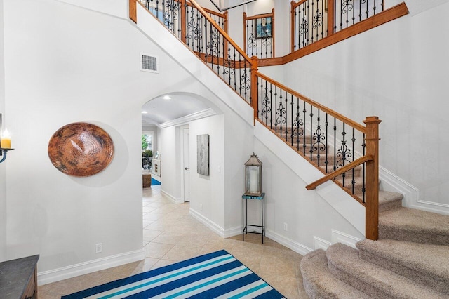 stairs with a towering ceiling, crown molding, and tile patterned flooring