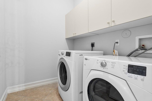 clothes washing area with washing machine and clothes dryer, light tile patterned floors, and cabinets