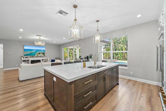 kitchen featuring decorative light fixtures, sink, light stone counters, a center island with sink, and dark brown cabinets