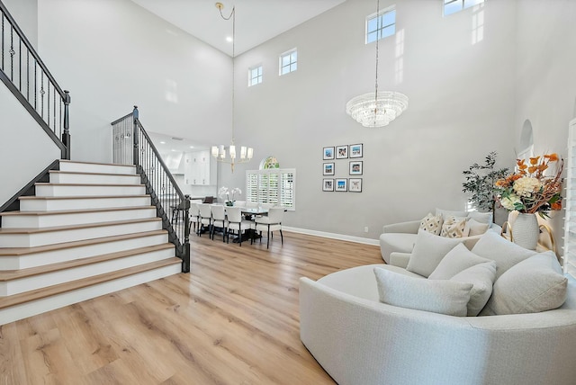 living room featuring a towering ceiling, a healthy amount of sunlight, an inviting chandelier, and wood-type flooring