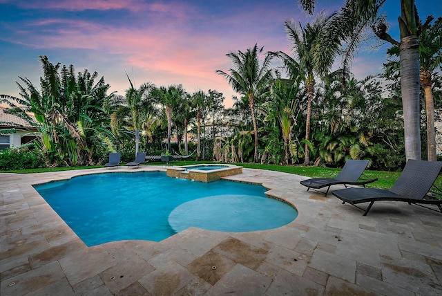 pool at dusk with an in ground hot tub and a patio area