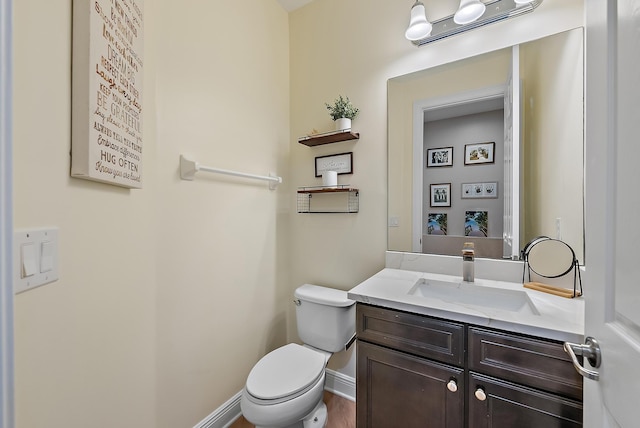 half bathroom featuring baseboards, toilet, and vanity
