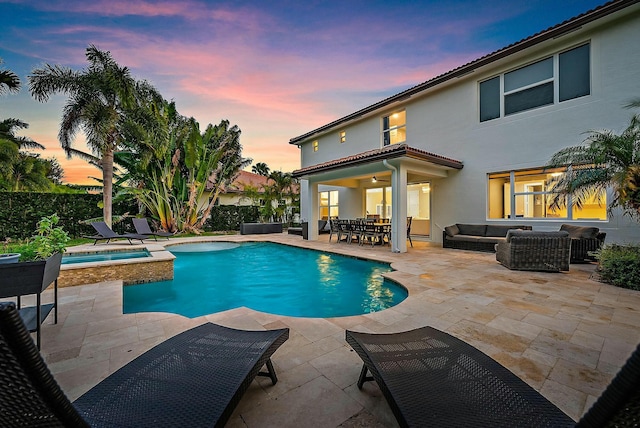 pool at dusk featuring outdoor lounge area, ceiling fan, an in ground hot tub, and a patio