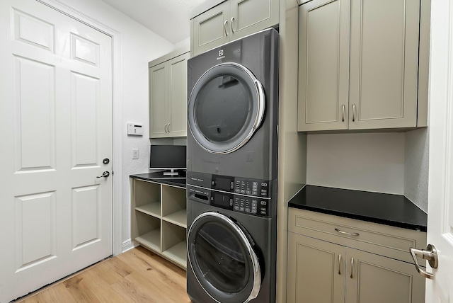 washroom with cabinets, light hardwood / wood-style flooring, and stacked washer and clothes dryer