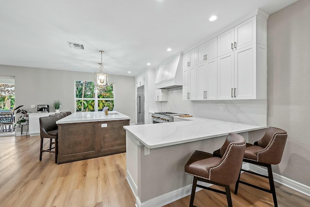 kitchen with pendant lighting, custom exhaust hood, white cabinetry, a kitchen island with sink, and a breakfast bar