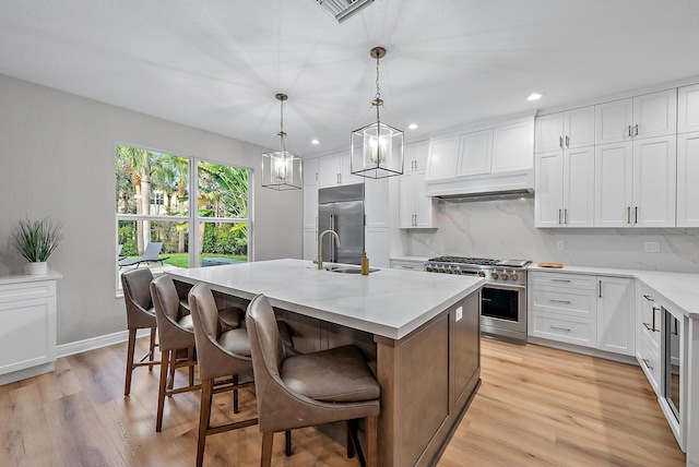 kitchen featuring premium appliances, decorative light fixtures, sink, white cabinetry, and an island with sink