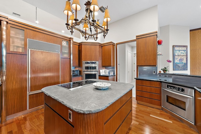 kitchen with brown cabinets, light wood-style floors, a center island, and a notable chandelier