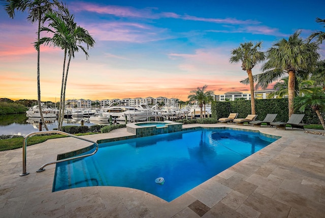 pool at dusk featuring an in ground hot tub, a patio, and a water view