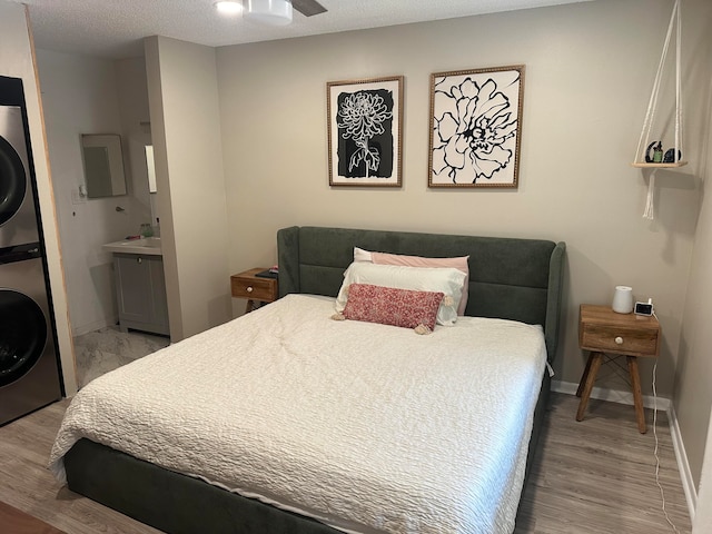 bedroom featuring stacked washing maching and dryer, connected bathroom, a textured ceiling, hardwood / wood-style floors, and ceiling fan