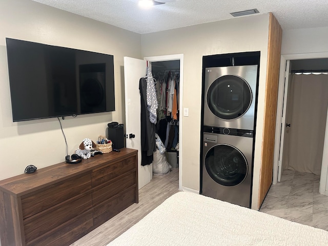 bedroom featuring a textured ceiling, a spacious closet, stacked washer / dryer, light hardwood / wood-style flooring, and a closet