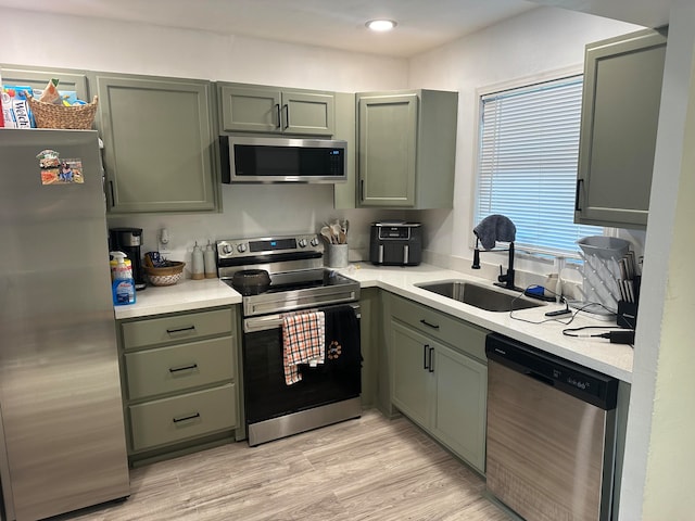 kitchen with appliances with stainless steel finishes, sink, green cabinetry, and light hardwood / wood-style flooring