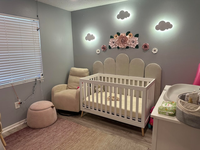 bedroom featuring a nursery area, wood-type flooring, and a textured ceiling