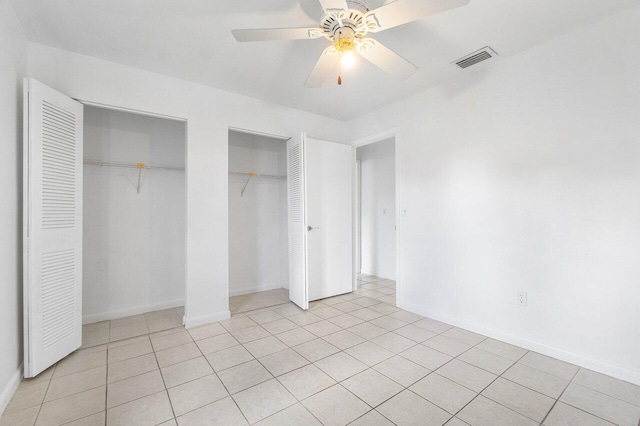 unfurnished bedroom featuring light tile patterned floors, ceiling fan, and two closets