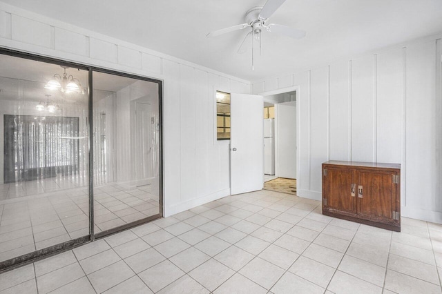 tiled spare room featuring ceiling fan with notable chandelier