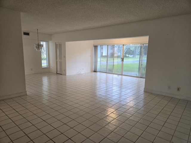 spare room featuring light tile patterned floors, a textured ceiling, a notable chandelier, visible vents, and baseboards