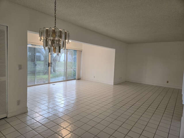 spare room featuring a textured ceiling, light tile patterned flooring, baseboards, and an inviting chandelier