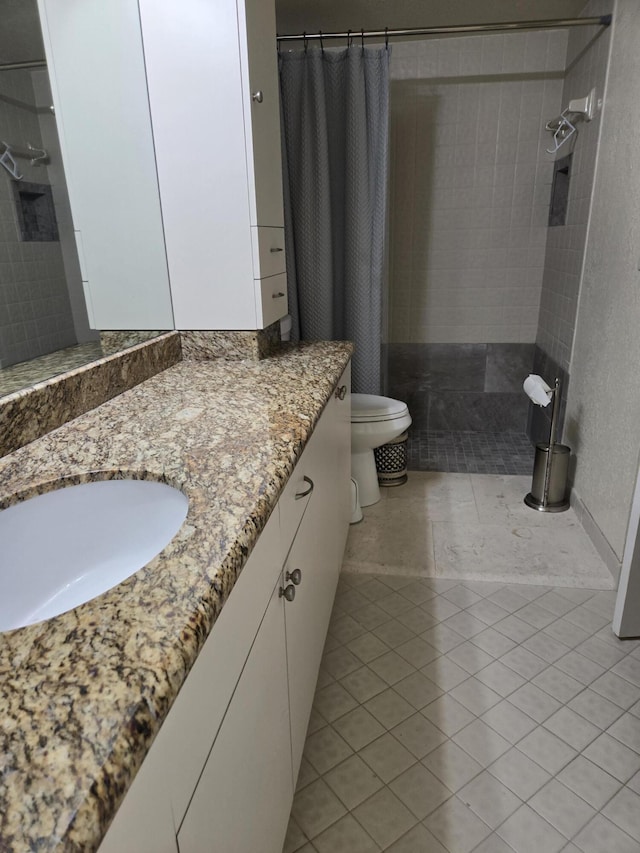 bathroom featuring toilet, tiled shower, tile patterned flooring, and vanity