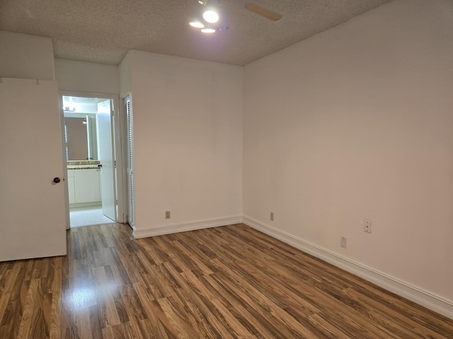 empty room with dark wood-type flooring, a textured ceiling, and baseboards