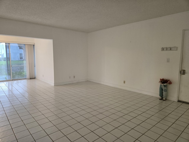 empty room with a textured ceiling, light tile patterned flooring, and baseboards