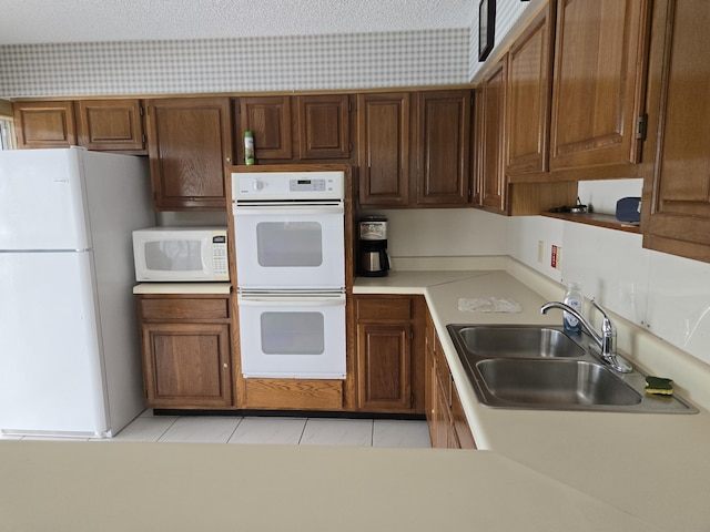 kitchen featuring light tile patterned floors, light countertops, white appliances, and a sink