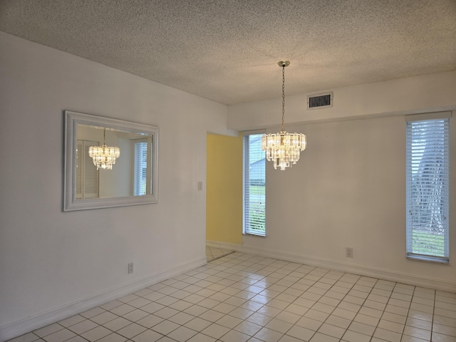 empty room featuring a textured ceiling, light tile patterned flooring, visible vents, baseboards, and an inviting chandelier