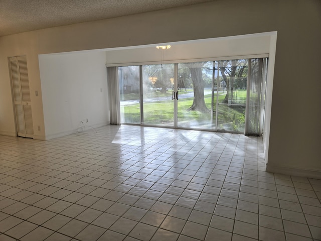 unfurnished room featuring a textured ceiling, light tile patterned floors, and baseboards