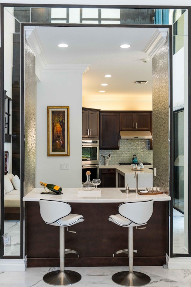 kitchen with backsplash, ornamental molding, dark brown cabinets, stainless steel double oven, and sink