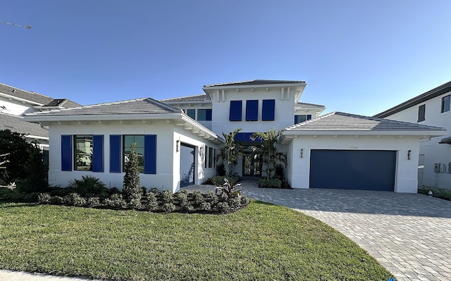 view of front facade featuring decorative driveway, a tile roof, stucco siding, an attached garage, and a front yard