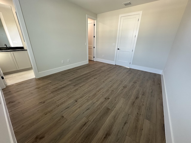 unfurnished room with dark wood-style floors, a sink, visible vents, and baseboards