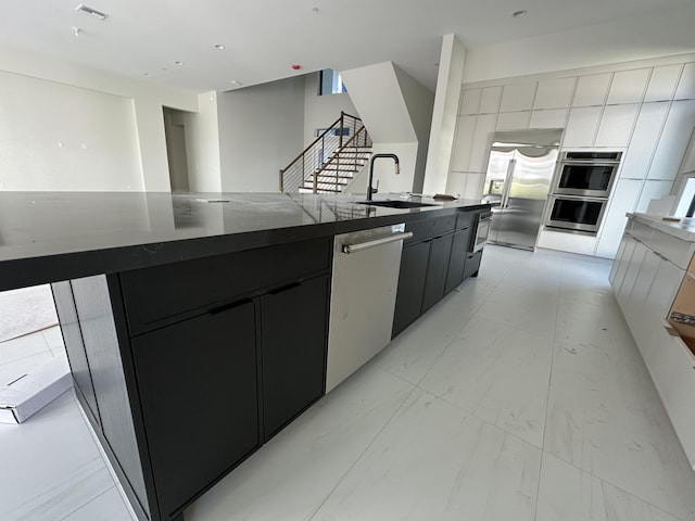 kitchen featuring marble finish floor, stainless steel appliances, a sink, modern cabinets, and dark cabinets