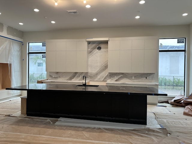 kitchen with sink, backsplash, white cabinetry, and an island with sink