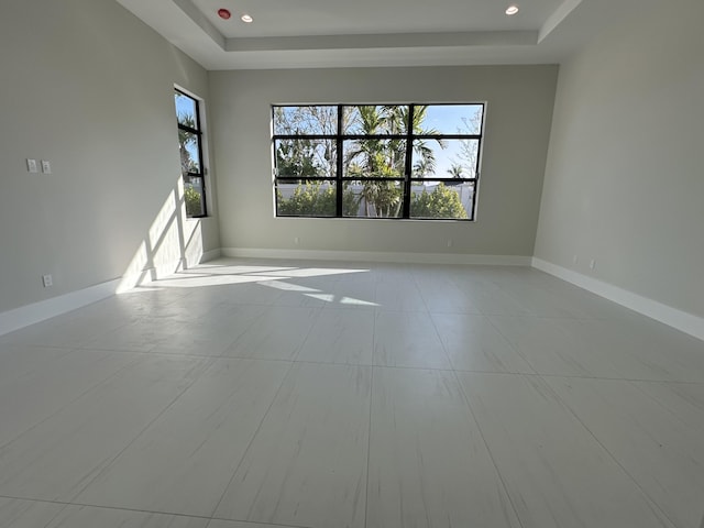 unfurnished room featuring a raised ceiling, plenty of natural light, and baseboards