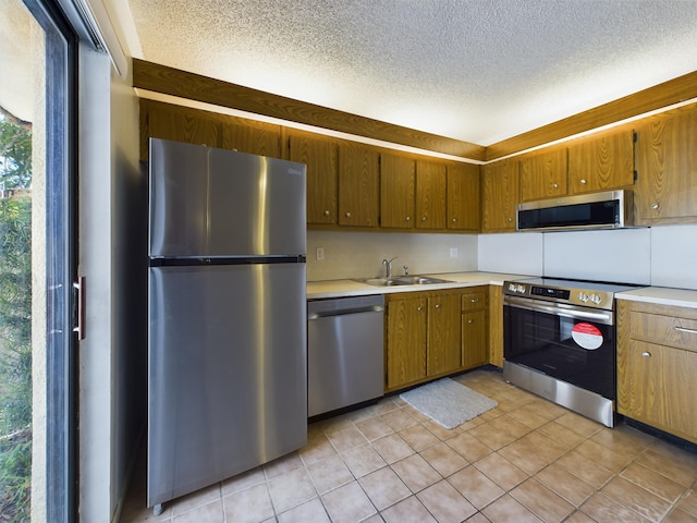 kitchen with a textured ceiling, appliances with stainless steel finishes, sink, and light tile patterned floors