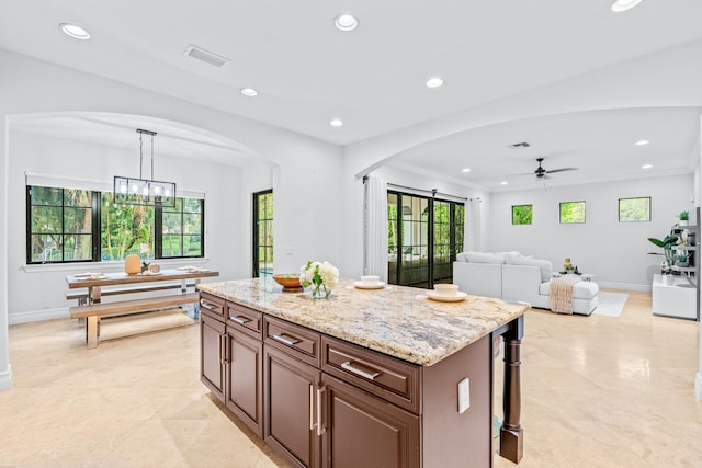 kitchen with a wealth of natural light, light stone countertops, decorative light fixtures, and a kitchen island