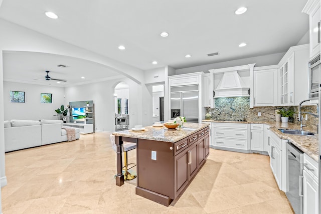 kitchen featuring built in appliances, white cabinetry, sink, a center island, and premium range hood