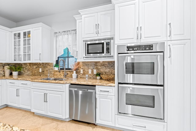 kitchen with stainless steel appliances, decorative backsplash, sink, light stone countertops, and white cabinetry