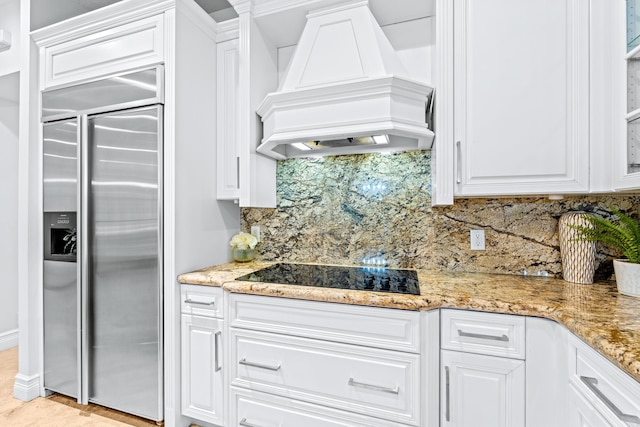 kitchen featuring black electric stovetop, built in fridge, backsplash, white cabinets, and custom exhaust hood