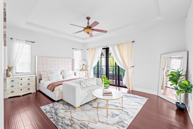 bedroom with dark wood-type flooring, access to outside, multiple windows, and a tray ceiling