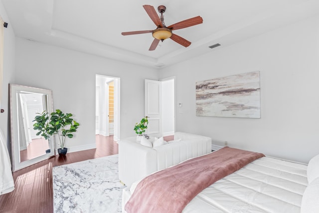 bedroom with dark wood-type flooring, ensuite bathroom, ceiling fan, and a raised ceiling