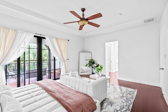 bedroom featuring ceiling fan, dark hardwood / wood-style floors, access to exterior, and a tray ceiling