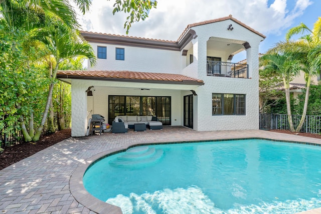 rear view of house with ceiling fan, a fenced in pool, a balcony, and outdoor lounge area