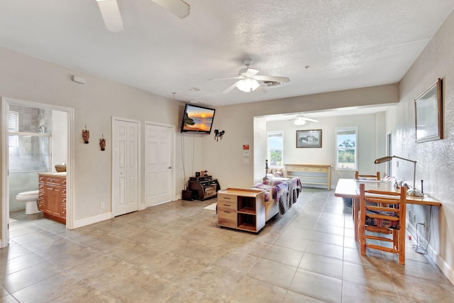 bedroom with a textured ceiling, two closets, ensuite bath, and ceiling fan