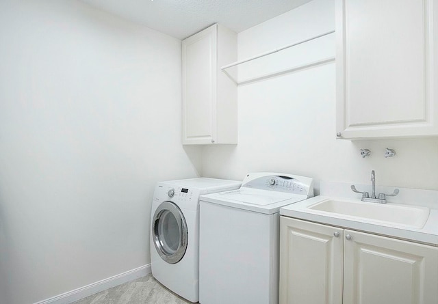 clothes washing area with washer and clothes dryer, cabinets, sink, and a textured ceiling