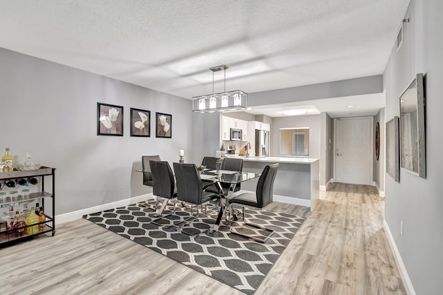 dining area with sink, a textured ceiling, and light wood-type flooring