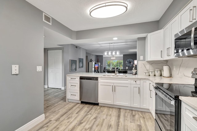 kitchen with pendant lighting, appliances with stainless steel finishes, sink, and white cabinets