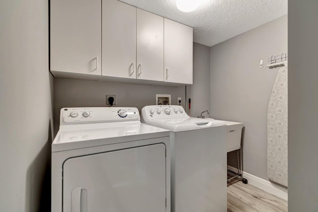 clothes washing area with cabinets, light wood-type flooring, a textured ceiling, and independent washer and dryer