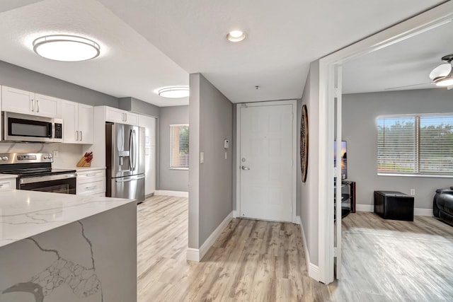 kitchen featuring ceiling fan, stainless steel appliances, light stone countertops, white cabinets, and light wood-type flooring