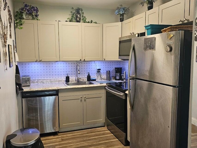 kitchen featuring stainless steel appliances, white cabinetry, light wood-type flooring, backsplash, and sink