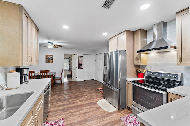 kitchen with appliances with stainless steel finishes, wall chimney range hood, tasteful backsplash, sink, and hardwood / wood-style flooring