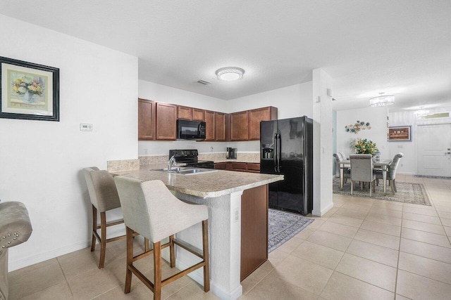 kitchen featuring light tile patterned flooring, sink, a breakfast bar area, kitchen peninsula, and black appliances